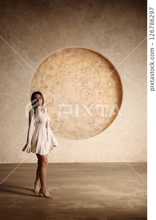 An Elegant Woman Wearing a Beautiful White Dress Stands Against a Large Circle Background An Elegant Woman Wearing a Beautiful White Dress Stands Against a Large Circle Background 126786297
