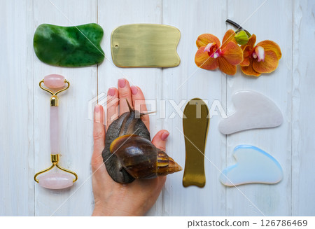 Spa concept gua sha massage body and face care and snails achatina on hand, flat lay. High quality photo Spa concept gua sha massage body and face care and snails achatina on hand, flat lay. High quality photo 126786469