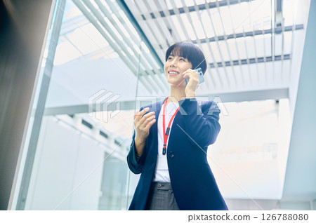 一位中年女商人在辦公室走廊上用智慧型手機打電話。 126788080