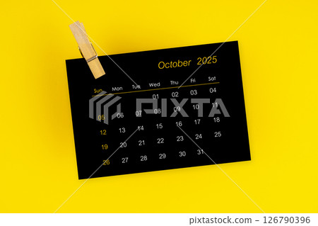 October 2025 black calendar with wooden clip on yellow background. 126790396
