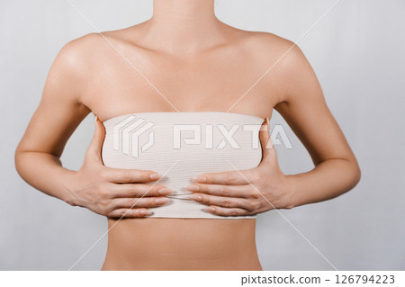 Patient Post-Breast Reduction: Woman Holding Bandaged Breasts While Recovering in Medical Setting 126794223