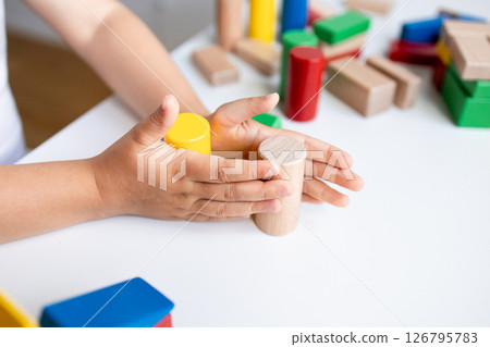 Child playing with colorful wooden building blocks on white table 126795783