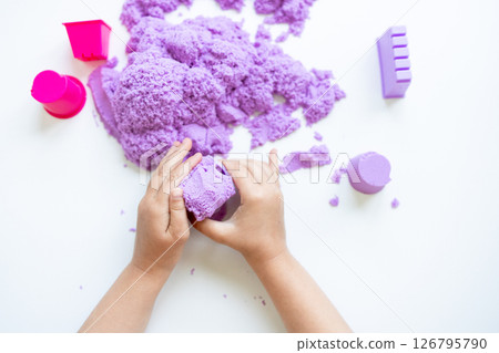 Child hands playing with purple kinetic sand on white surface 126795790