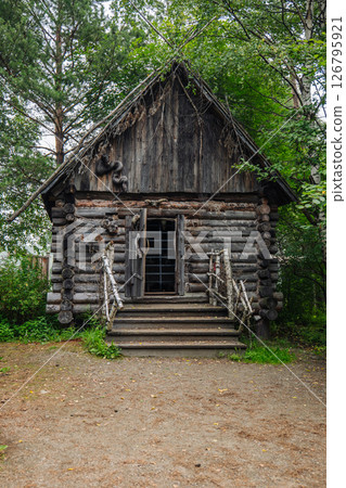 Weathered wooden hut with barred entrance standing among dense forest trees, embodying haunting russian folklore atmosphere Weathered wooden hut with barred entrance standing among dense forest trees, embodying haunting russian folklore atmosphere 126795921