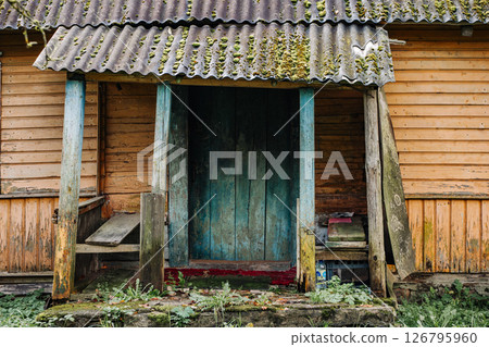Old abandoned wooden house with moss covered roof and weathered blue door Old abandoned wooden house with moss covered roof and weathered blue door 126795960