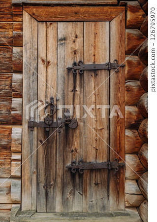 Weathered wooden door featuring rusted metal hinges, revealing aged craftsmanship within vintage log cabin interior 126795970
