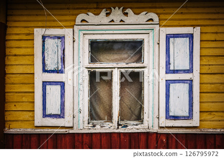 Old weathered window with decorative shutters on a yellow wooden facade is showing signs of decay 126795972