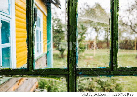 Old window with peeling green paint showing colorful house and garden 126795985