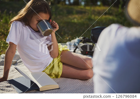 Young Girl Sipping from a Mug While Relaxing Outdoors with a Book 126796084