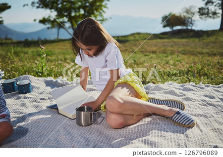 Young Girl Enjoys Reading Outdoors During a Summer Picnic in Scenic Mountain Setting Young Girl Enjoys Reading Outdoors During a Summer Picnic in Scenic Mountain Setting 126796089