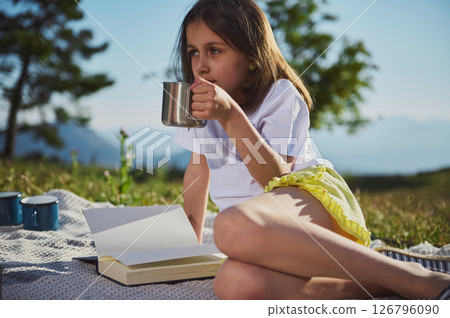 Young Girl Enjoying an Outdoor Picnic Reading a Book and Sipping a Beverage, Surrounded by Nature's Beauty Young Girl Enjoying an Outdoor Picnic Reading a Book and Sipping a Beverage, Surrounded by Nature's Beauty 126796090