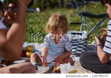 Outdoor Family Picnic with Children Enjoying Food and Togetherness in a Scenic Green Setting 126796147