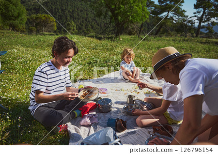 Family Enjoying a Picnic Outdoors in a Scenic Mountain Landscape Family Enjoying a Picnic Outdoors in a Scenic Mountain Landscape 126796154
