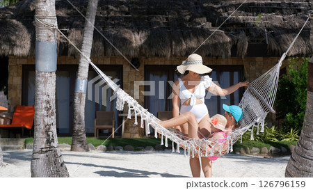 Mom swings daughters in hammock on tropical beach enjoying sunny vacation Mom swings daughters in hammock on tropical beach enjoying sunny vacation 126796159