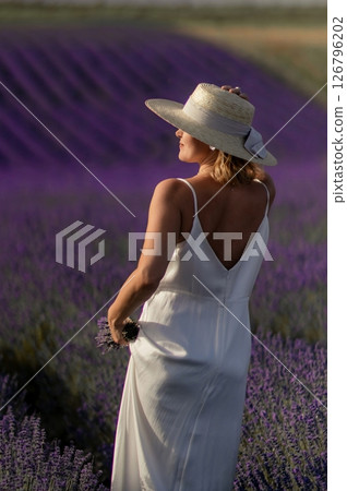A woman wearing a straw hat stands in a field of lavender 126796202