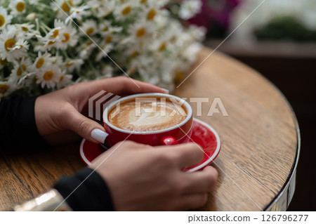 Cappuccino Flowers Cafe: Hands hold latte art cappuccino at cafe today, enjoying flowers for a relaxing moment. Cappuccino Flowers Cafe: Hands hold latte art cappuccino at cafe today, enjoying flowers for a relaxing moment. 126796277