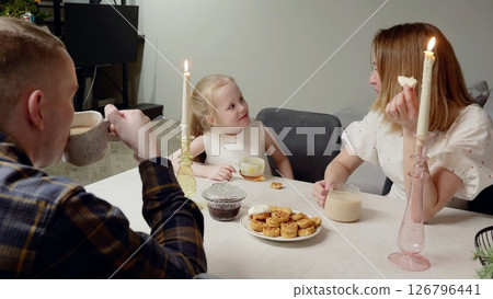 Family sharing festive breakfast, parents and child enjoying waffles, hot chocolate, candlelight creating warm holiday morning atmosphere at home Family sharing festive breakfast, parents and child enjoying waffles, hot chocolate, candlelight creating warm holiday morning atmosphere at home 126796441