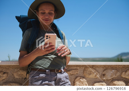 Traveler Enjoying Outdoor Adventure Checking Smartphone in Scenic Countryside Location Traveler Enjoying Outdoor Adventure Checking Smartphone in Scenic Countryside Location 126796916