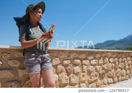 Hiker Relaxing by Stone Wall with Scenic Mountain Views Under Clear Blue Sky 126796917