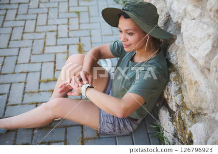 Woman Relaxing Outdoors Wearing Hat and Green Casual Outfit 126796923
