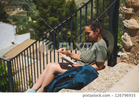 Traveler Relaxing While Reading a Book Outdoors in a Scenic Rural Landscape 126796935