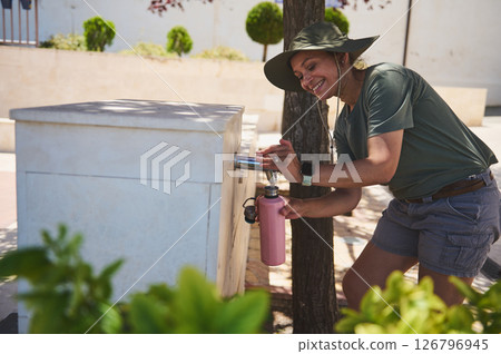 Person Refilling Water Bottle at Outdoor Fountain During A Scenic Day 126796945