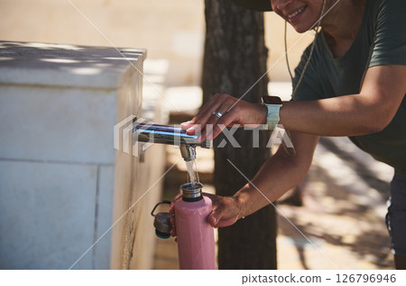 Woman Refilling Water Bottle at Public Fountain Outdoors on a Sunny Day Woman Refilling Water Bottle at Public Fountain Outdoors on a Sunny Day 126796946