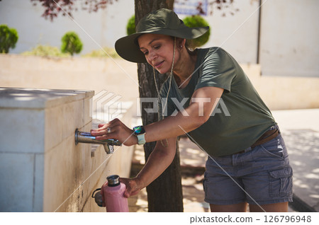 Traveler Refilling Water Bottle at Outdoor Fountain on a Sunny Day 126796948