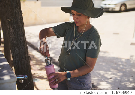 Person Filling Pink Reusable Bottle at Outdoor Water Tap 126796949