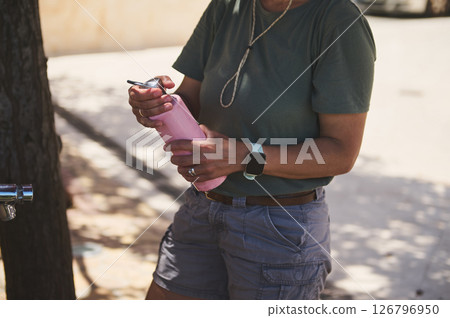Adult Holding Pink Water Bottle While Outdoors on a Sunny Day 126796950