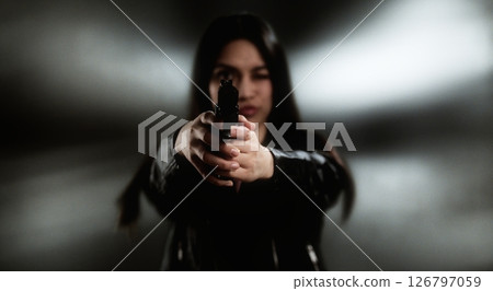 Young woman aiming with a handgun in a blurred background 126797059