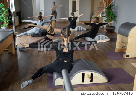 Woman doing mermaid exercise on back spine corrector. Reformer pilates studio machine for fitness workouts in gym. Fit, healthy and strong authentical body. Fitness concept. 126797410