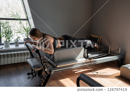 Woman doing Swan exercise on Pilates Reformer for the chest and back muscles, focusing on flexibility, strength, and control with determination 126797419