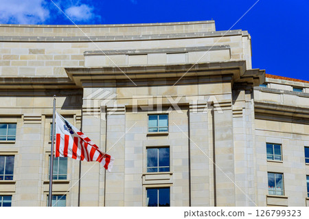19 April 2025 Washington D.C US Bright sunlight highlights modern architecture of government building, with an American flag proudly waving. 126799323