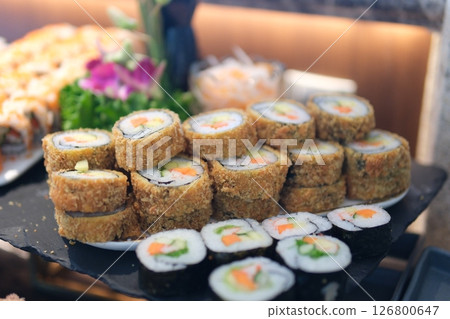 Fried sushi rolls topped with creamy filling, spoon adding garnish, crispy crust, vibrant colors, professional presentation, food preparation closeup 126800647