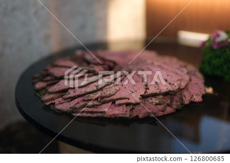 Caucasian man hand puts plastic package with circles of thinly sliced ham on table. Plastic packaging for chopped snacks on stone. Sliced into thin pieces of ham on cutting serving board. Slow motion 126800685