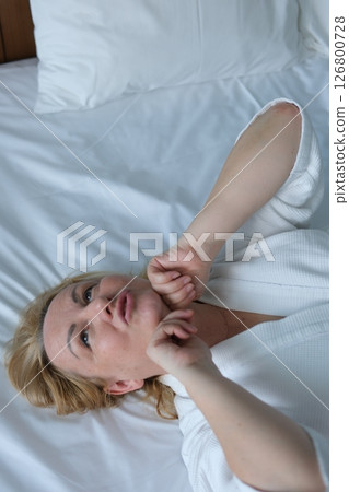 woman doing facial massage lying on white sheet massaging forehead chin rubbing hands youth beauty adult woman taking care of herself at home european female in white coat 126800728