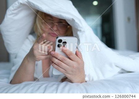 adult woman under blanket with phone rest at home lying on elbows lies wrap cover blanket duvet on pillow use mobile cell phone isolated on pastel blue background Night bedtime concept adult woman under blanket with phone rest at home lying on elbows lies wrap cover blanket duvet on pillow use mobile cell phone isolated on pastel blue background Night bedtime concept 126800744