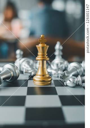 A golden chess king stands triumphantly surrounded by fallen silver pieces on a chessboard, symbolizing strategy and victory. A golden chess king stands triumphantly surrounded by fallen silver pieces on a chessboard, symbolizing strategy and victory. 126801147