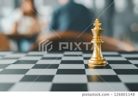 Close-up of a golden chess king on a checkered board with a blurred background, symbolizing strategy and leadership. 126801148