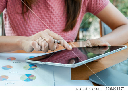 Professional woman using a tablet to review business charts and graphs, highlighting digital technology in a modern workspace. 126801171