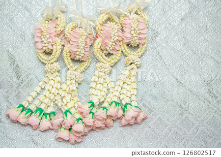 Beautiful Thai-style jasmine garland on a silver cloth background with an ancient Thai pattern. Beautiful Thai-style jasmine garland on a silver cloth background with an ancient Thai pattern. 126802517