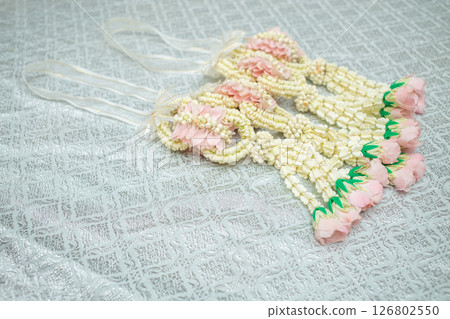 Beautiful Thai-style jasmine garland on a silver cloth background with an ancient Thai pattern. Beautiful Thai-style jasmine garland on a silver cloth background with an ancient Thai pattern. 126802550