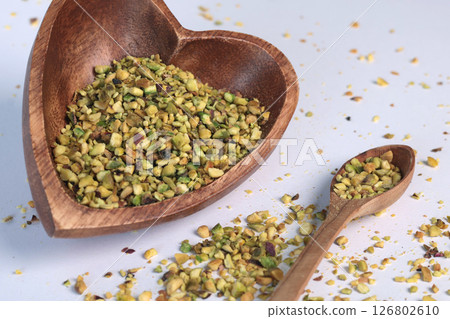 Crushed pistachio nuts in wooden bowl and heart-shaped spoon for cooking. Environmentally friendly product and health. 126802610