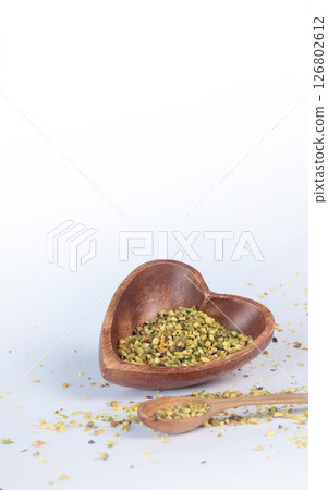 Crushed pistachio nuts in wooden bowl and heart-shaped spoon for cooking. Environmentally friendly product and health. 126802612