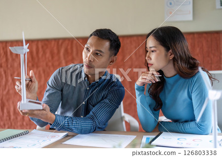 ESG Business Collaboration. Two professionals discussing renewable energy models in a modern office. ESG Business Collaboration. Two professionals discussing renewable energy models in a modern office. 126803338