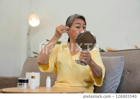 Beauty and Skincare Routine. An elderly woman applying serum in front of a mirror, embracing her beauty. Beauty and Skincare Routine. An elderly woman applying serum in front of a mirror, embracing her beauty. 126803340