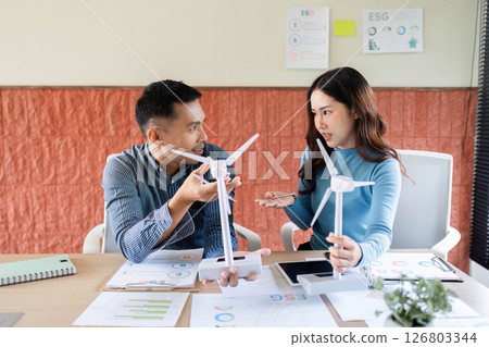 ESG Strategy Meeting. Colleagues discussing renewable energy initiatives using wind turbine models. ESG Strategy Meeting. Colleagues discussing renewable energy initiatives using wind turbine models. 126803344