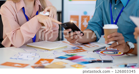 Design Team Engaging in Creative Process. Professionals analyzing designs and discussing ideas at a collaborative workspace. 126803345