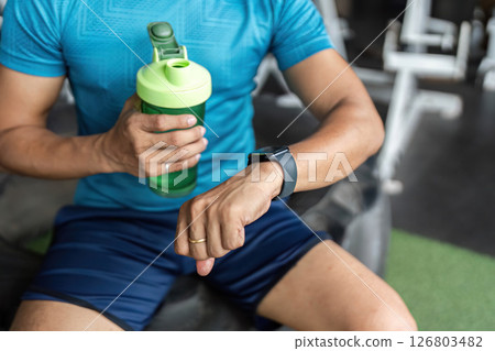 Fitness Routine: Man Hydrating with Water Bottle and Smartwatch in Gym 126803482